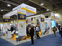 The Australia Minerals booth viewed from the side, showing archways with posters and a large hanging sign both displaying new branding, and a large video wall