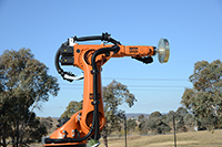 Photo of the large orange robot in the process of performing a test on a GNSS antenna.