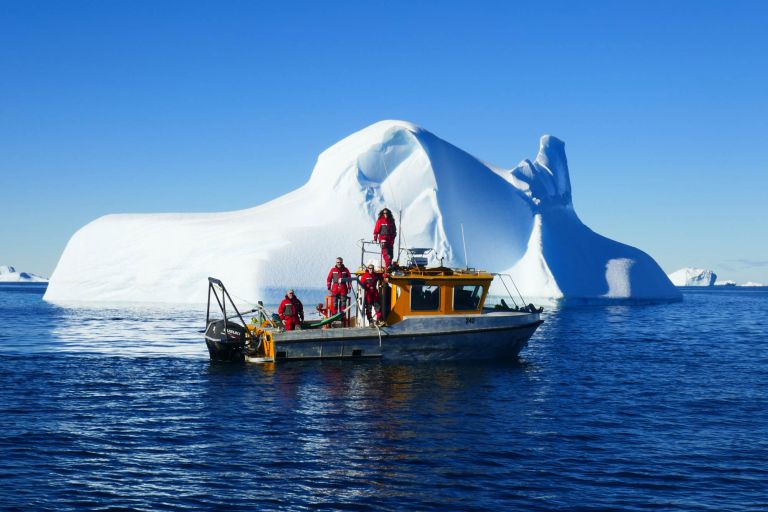 Researchers conducting marine fieldwork from a survey boat near an iceberg in Antarctic waters