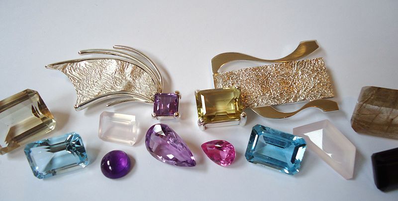 A variety of cut, coloured  gemstones and some ornate shiny metal brooches