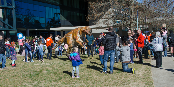 Crowds of adults and children surrounding a large puppet dinosaur