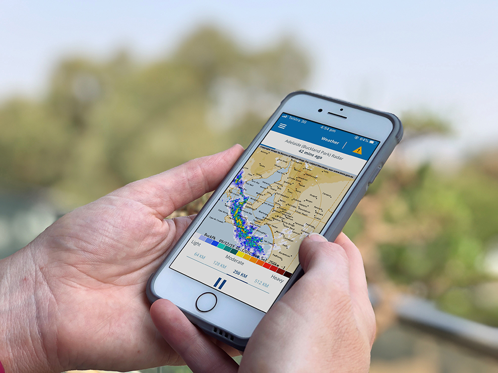 A person holding a mobile phone using the Bureau of Meteorology (BOM) app.