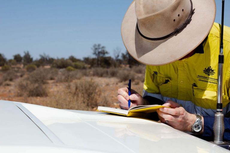 man writing in notebook on car bonnet