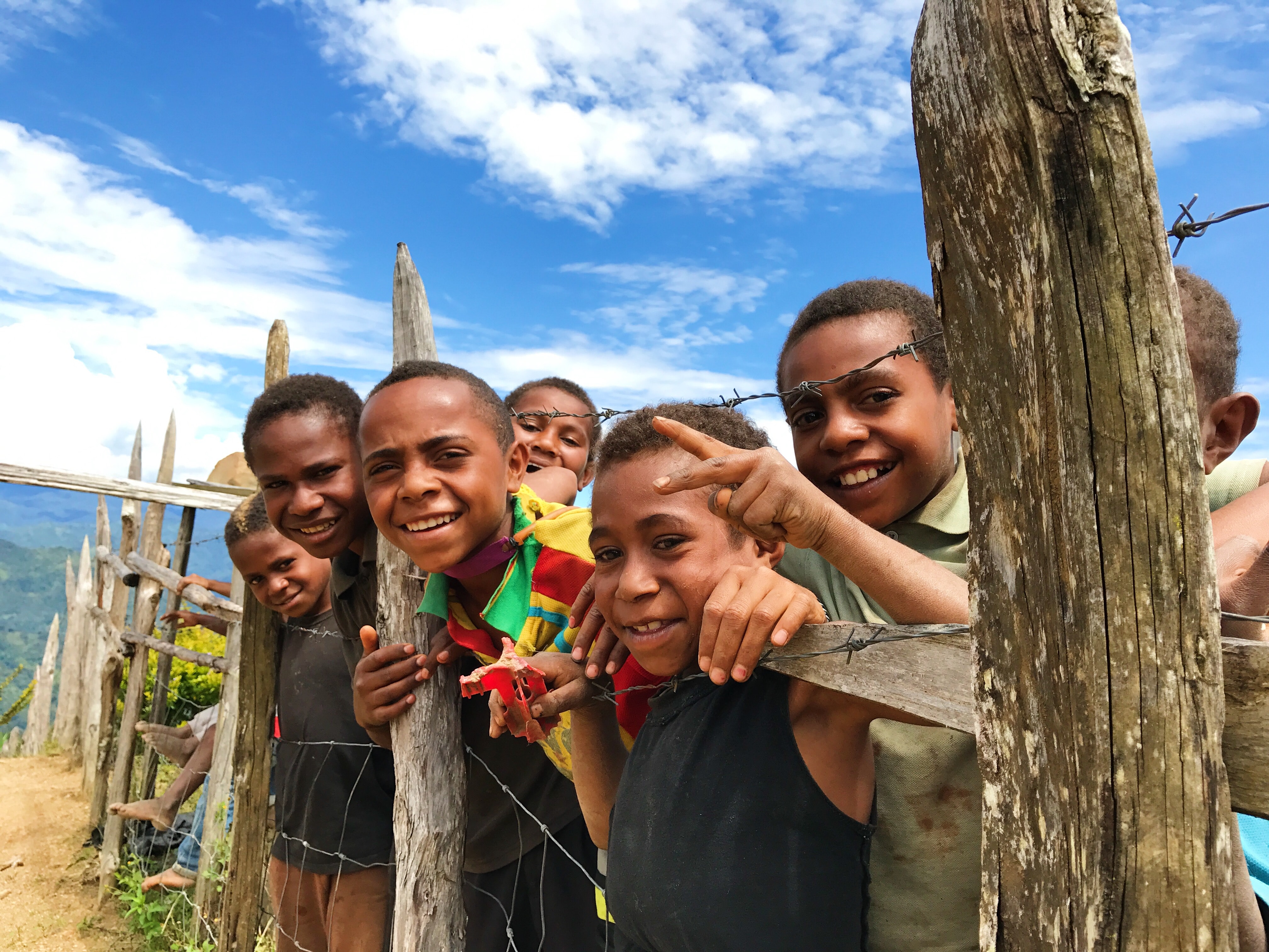 A group of smiling children standing along a barbwire fence in PNG
