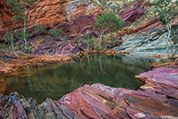 Red colour rock layers and trees surrounding a waterhole