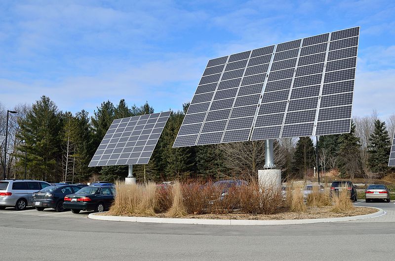 Two solar panel arrays mounted on steel pylons with concrete bases in a car park