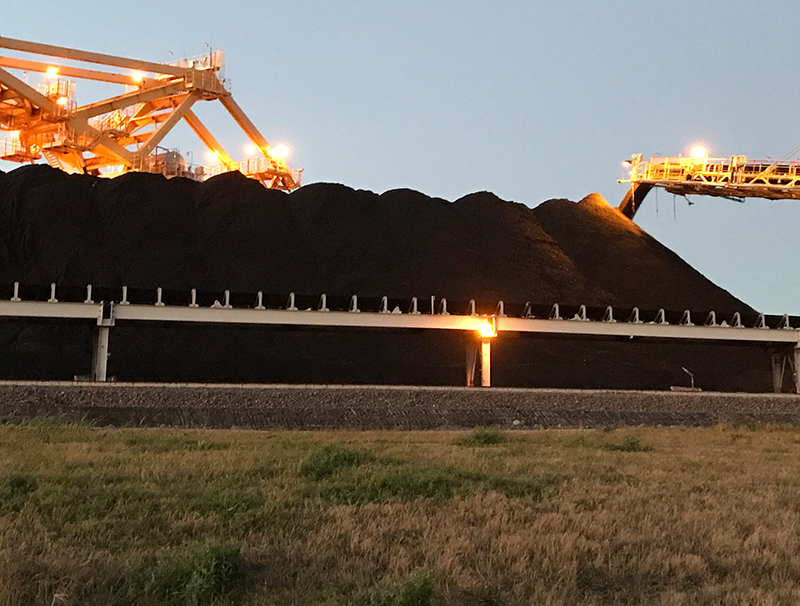 Black coloured coal is coming off a long conveyer onto a large pile of coal