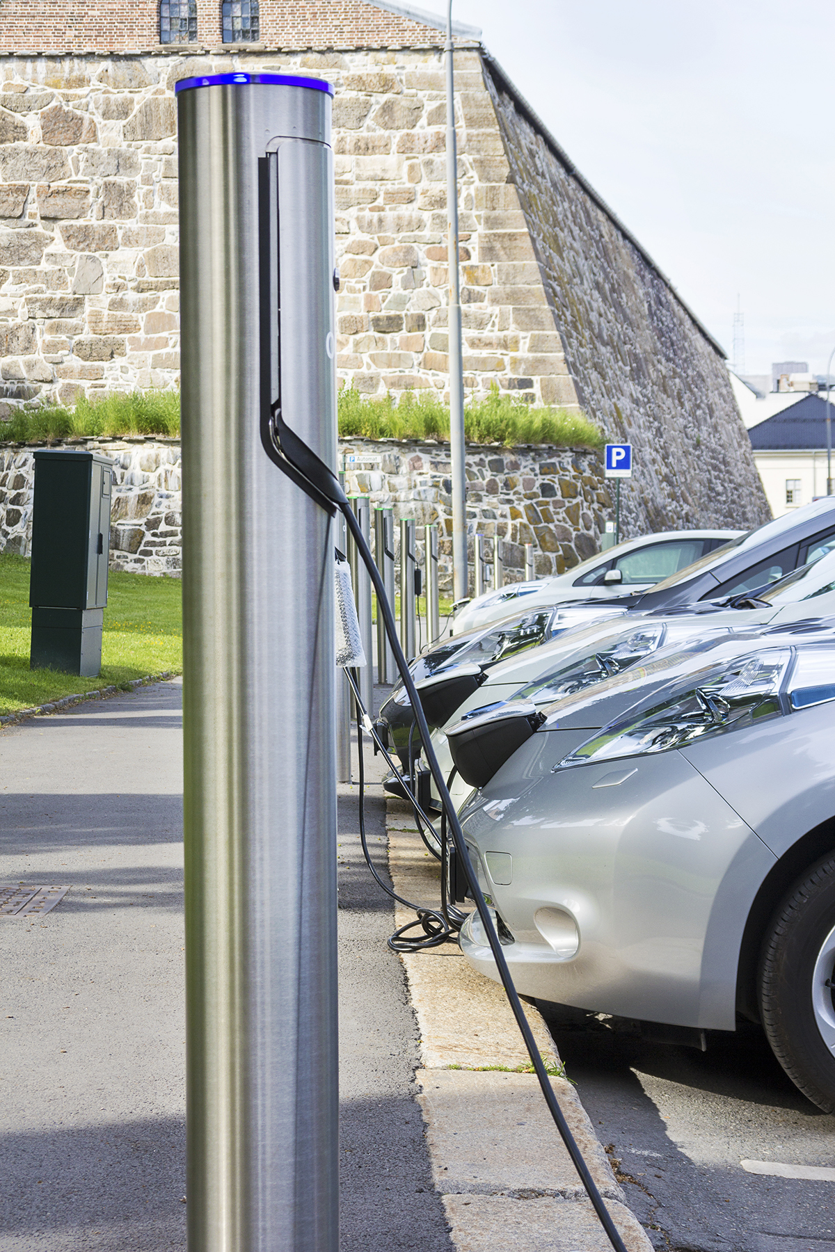 A row of electric vehicles connected to public re-charging stations in a scenic car park.