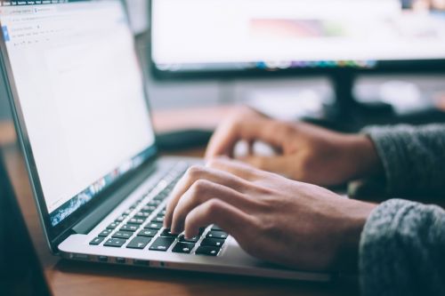 Close-up of hands typing on a laptop computer, representing access to digital coastal maps, data and online information