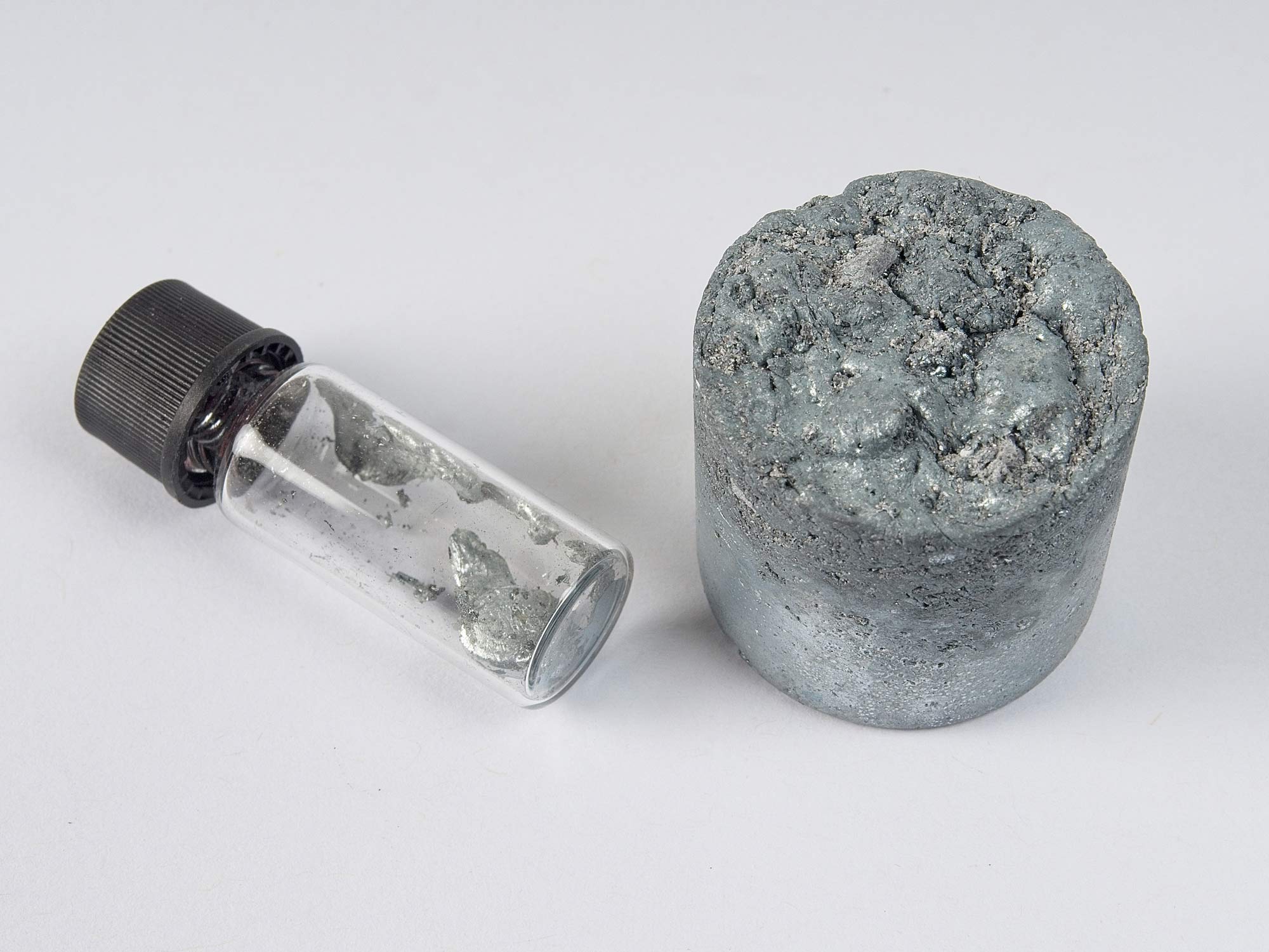 A sample bottle with a small piece of a grey, metallic substance, and a larger, cylindrical piece next to it. This is a critical mineral called Gallium.