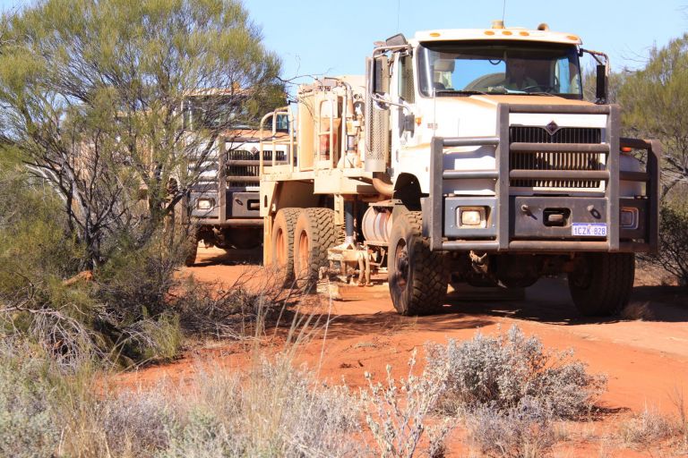 Front side view of trucks in remote landscape with trees and bushes on either side