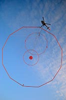 An image showing the Geotech VTEM FullWaveForm airborne electromagnetic (AEM) acquisition system suspended beneath a Eurocopter A350B helicopter. The AEM transmitter is a large loop of wire in a circular frame at bottom, the receiver is a small loop of wire in the centre of the large loop. A magnetometer and other flight instruments are attached to a smaller loop above the receiver loop