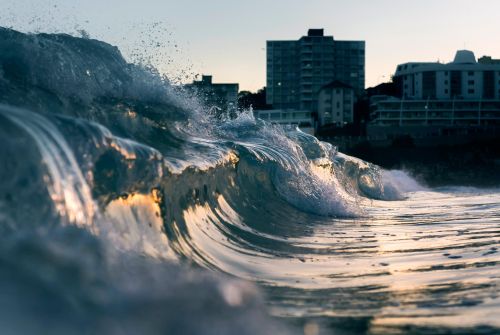 Breaking ocean wave approaching an urban coastline at sunset