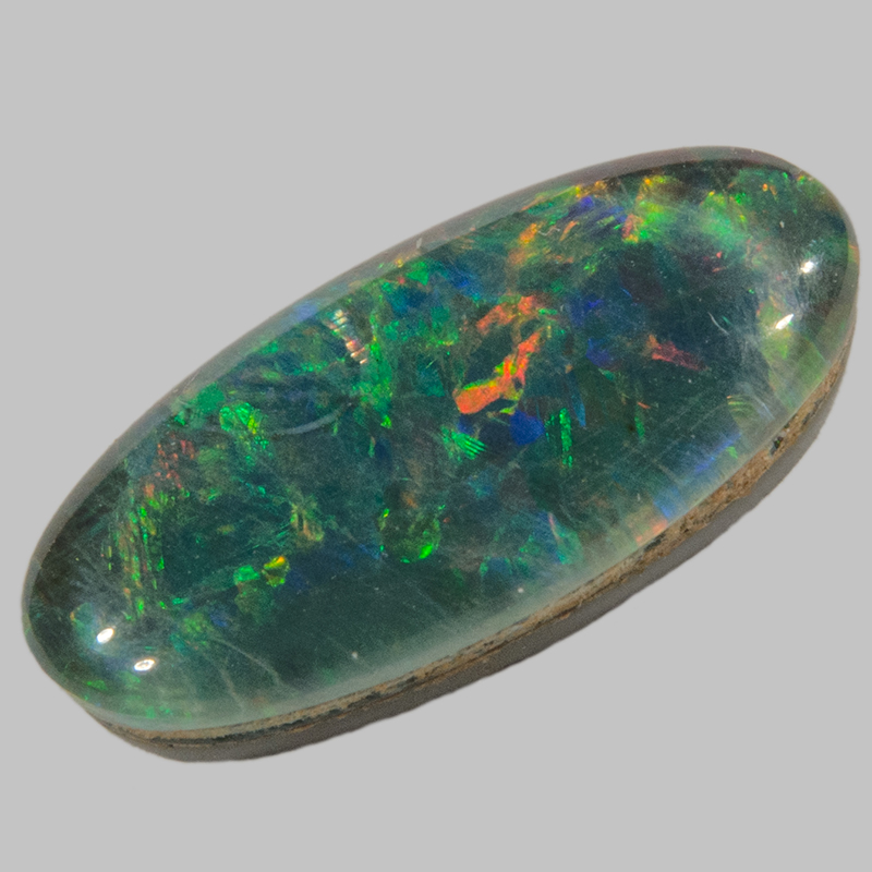 Rounded colourful opal gemstone sliver mounted on a dark coloured base, with a transparent cover