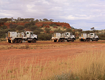 Three large trucks with arid hills of the Flinders Ranges in the background