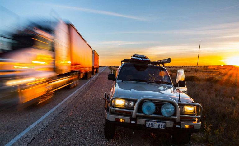 Road train rushing past car parked on the side of the Nullarbor Plain highway