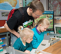 Geoscience Australia staff member interacting with two young visitors looking through a microscope.