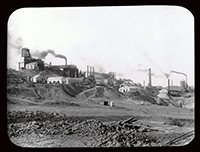 An archival black and white photo of buildings and a mining operation on a hill