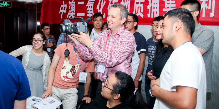 A group of workshop participants gather around scientist holding a carbon dioxide video camera