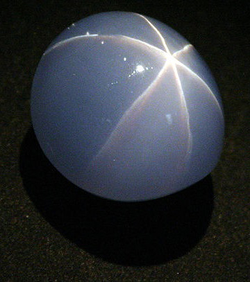 Pale blue cloudy looking sapphire gemstone with a white lines, forming a star shape on its surface.