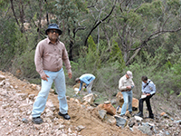 A photo of four scientists examining rocks on the side of a hill during fieldwork