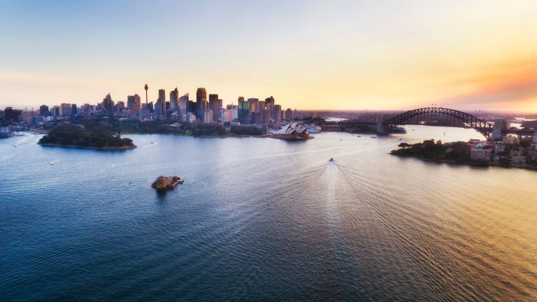 Colourful sunset over Sydney city CBD and harbour landmarks in elevated aerial view above Harbour waters.