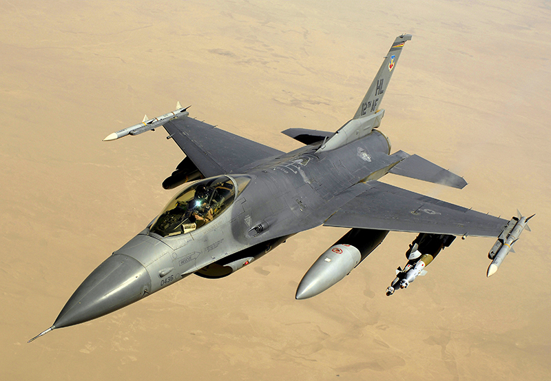 A silver coloured F-16 fighter aircraft in flight