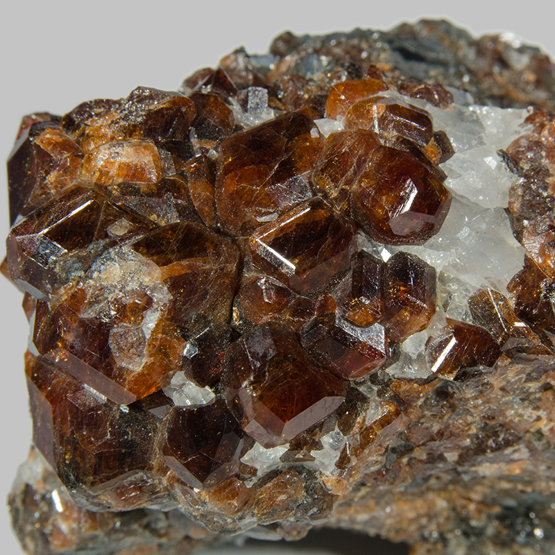 A cluster of transparent, orange coloured spessartine crystal in an orange and grey rock.