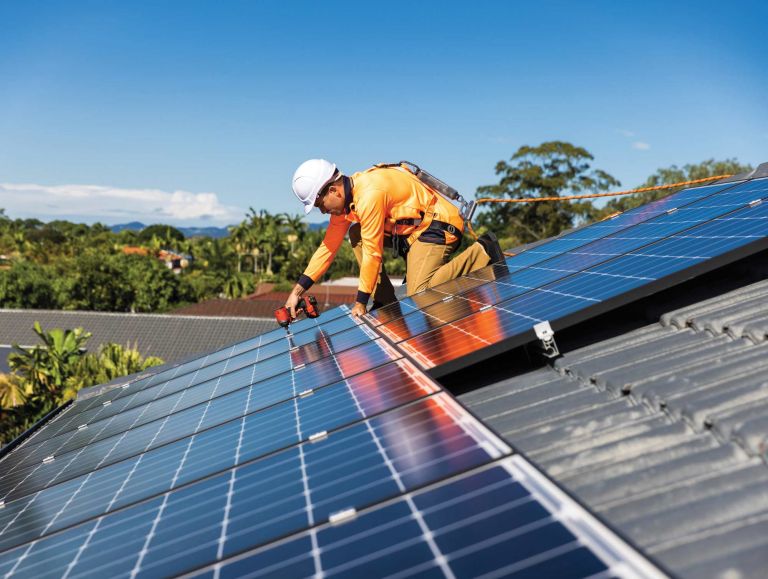 Solar panel technician with drill installing solar panels on house roof on a sunny day.