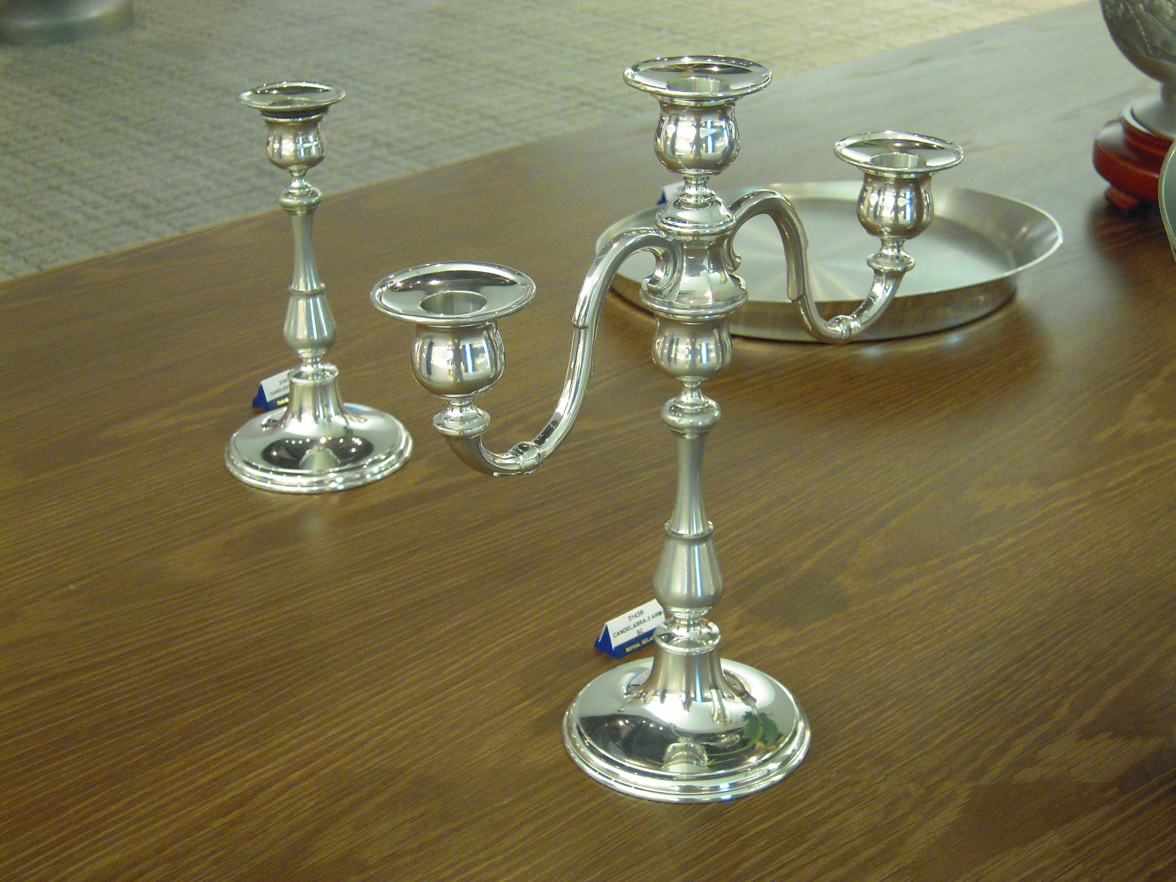 Two ornate, shiny, silver coloured, candlesticks and a silver coloured plate on a wooden table