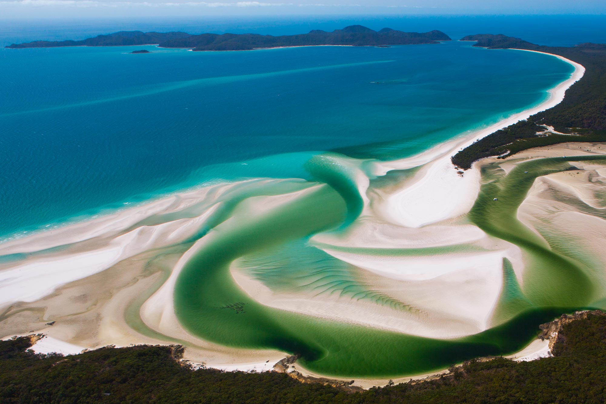 Aerial view of a sweeping Australian coastline with turquoise water, white sandbanks, tidal channels and forested headlands, Whitehaven Beach, Queensland