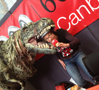 A radio presenter being playfully eaten by a puppet dinosaur.