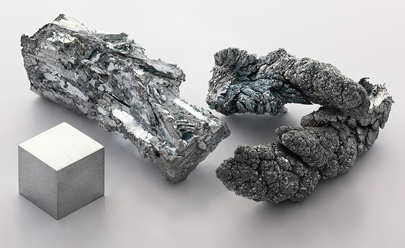 A silver coloured zinc cube beside an irregularly shaped silver coloured crystal and a silver-grey coloured mineral with dendritic form