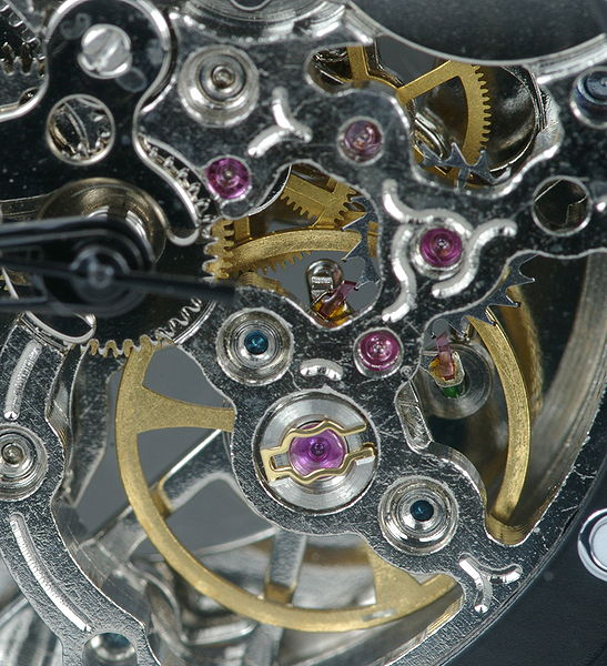 Metal and plastics watch workings with springs, discs and and small wheels. Pink coloured ruby crystals are embedded in some of the metal discs
