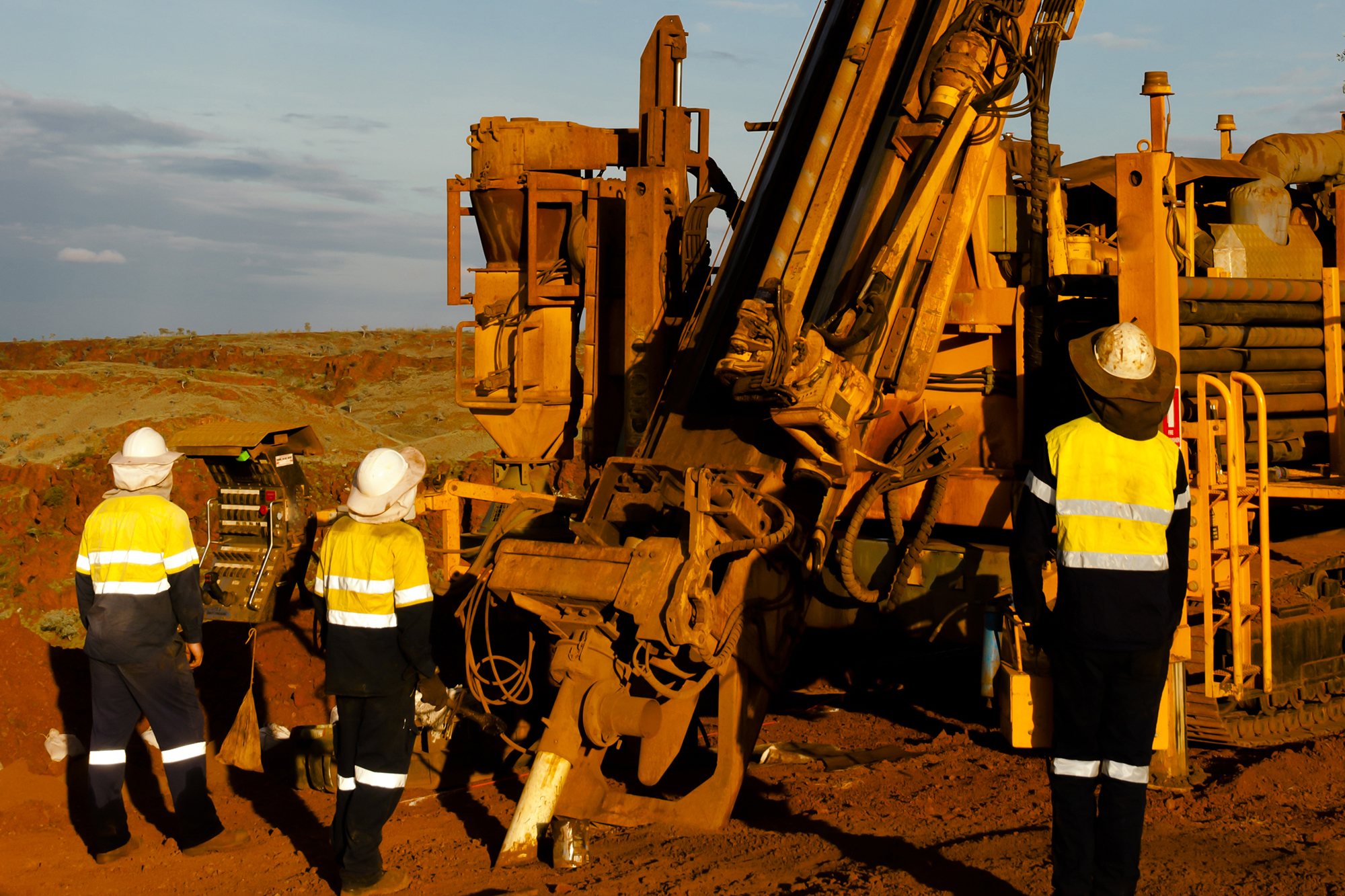 Three employees operating an exploration drill rig in the outback Pilbara region of Australia.