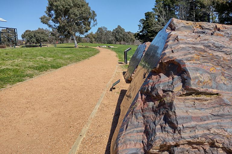 The TimeWalk walking track is a wide gravel path with wooden borders. There are rocks and signage to the side of the path.