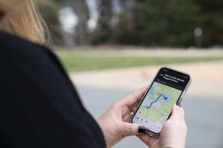 Photograph showing a person holding a smartphone displaying a navigation app with a blue route highlighted on a map. The screen indicates directions for a trip to