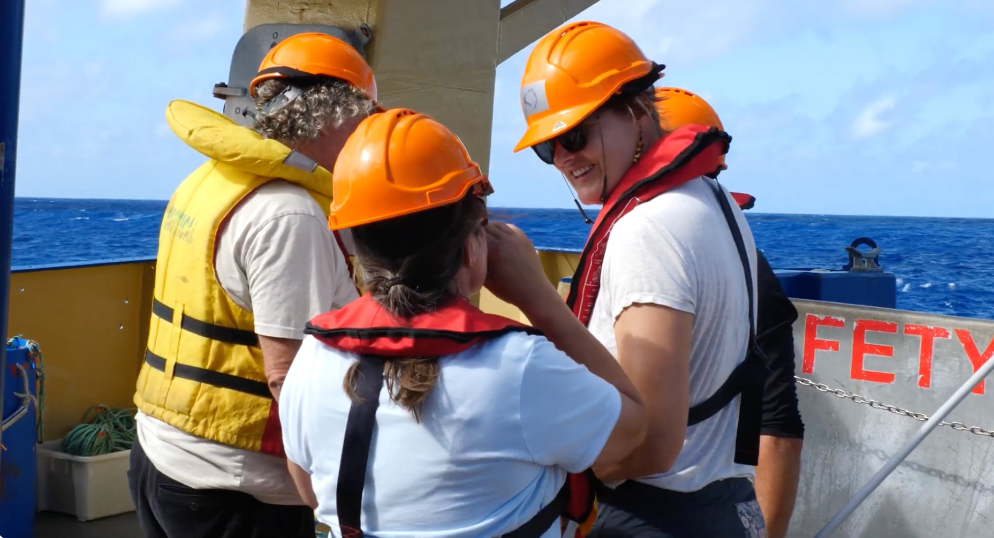 Researchers wearing safety equipment collaborate on the deck of a research vessel during a seabed survey