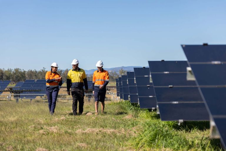 Three people in hi vis walking through solar farm.