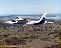 Aeroplane flying over farmland scattered with vegetation.