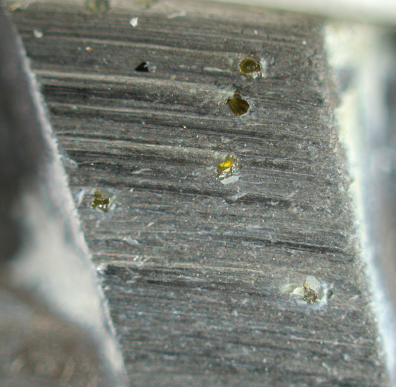 A close up of small yellow diamond crystals embedded in a silver coloured metallic blade surface