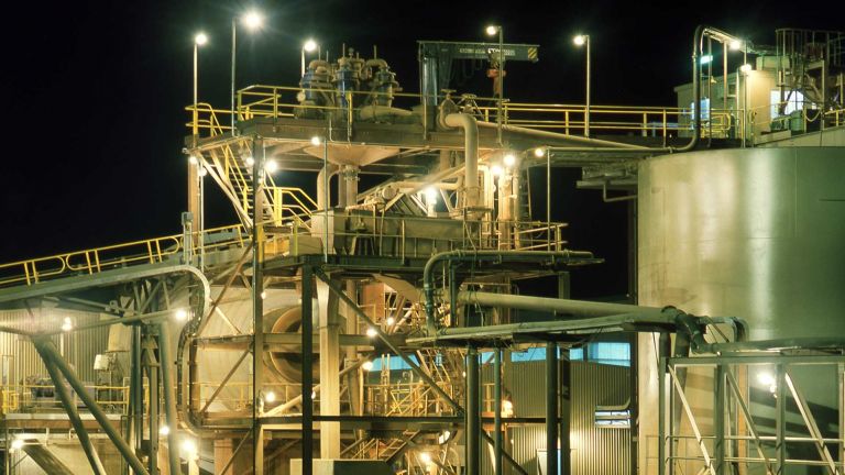 Gold mine processing plant at night with tailings dam in foreground.