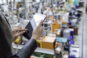 A woman standing on a balcony in a futuristic factory using a digital tablet.