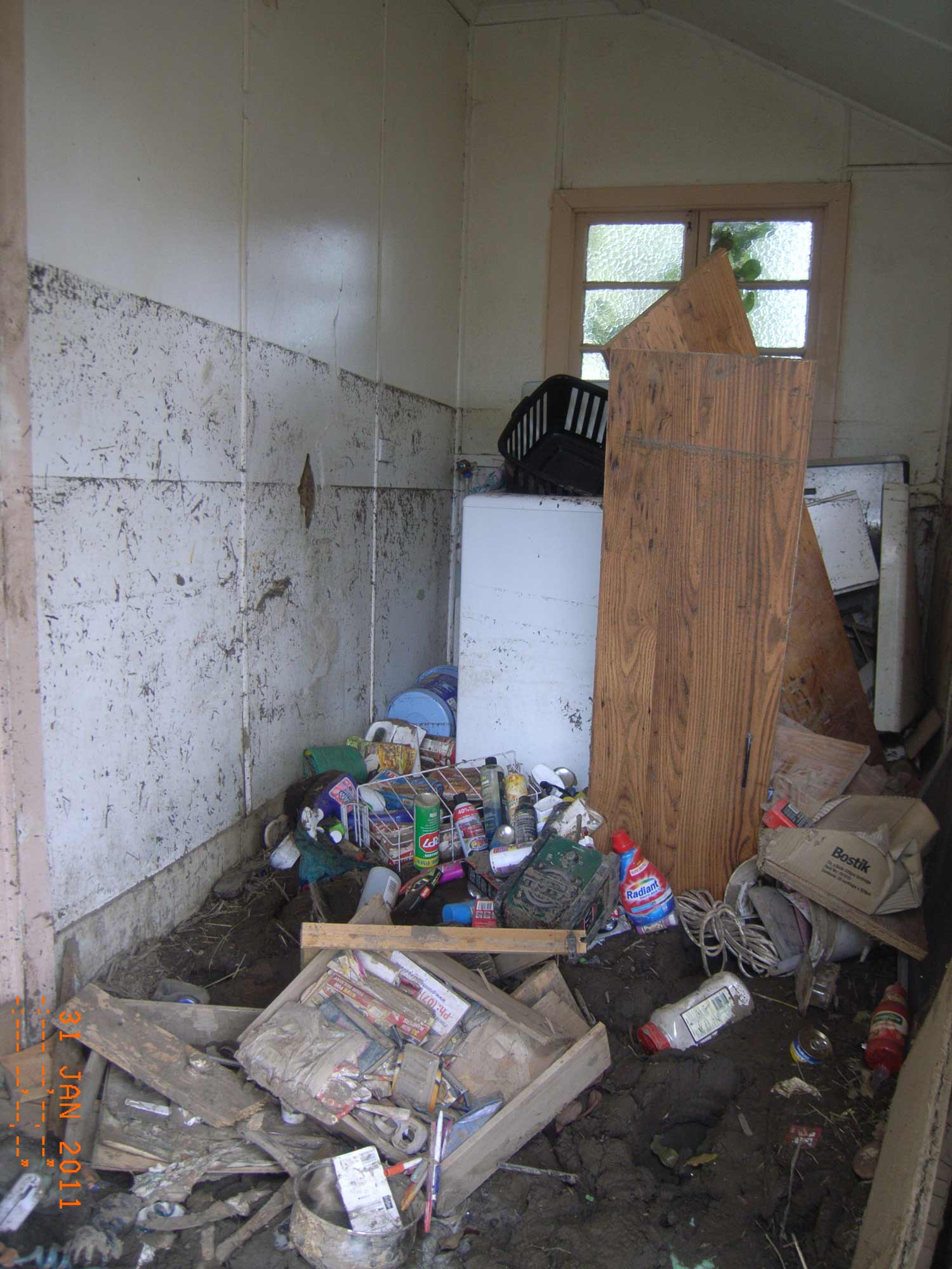 Image of house interior, showing dirty water marks up the internal walls, and rubble on the ground.