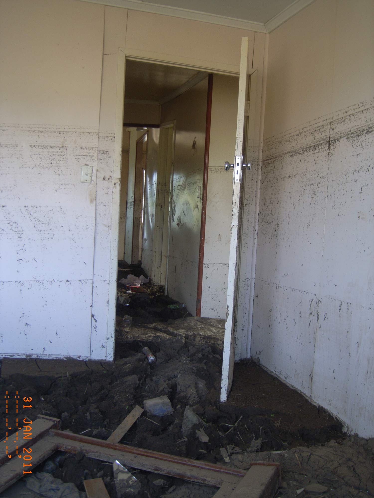 Image of house interior, showing dirty water marks up the internal walls, and rubble on the ground.