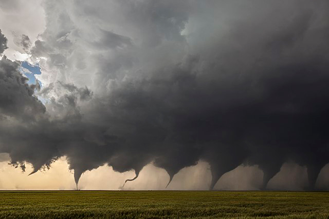 From left to right, a tornado forms from the clouds, touches the ground, and grows significantly in size.
