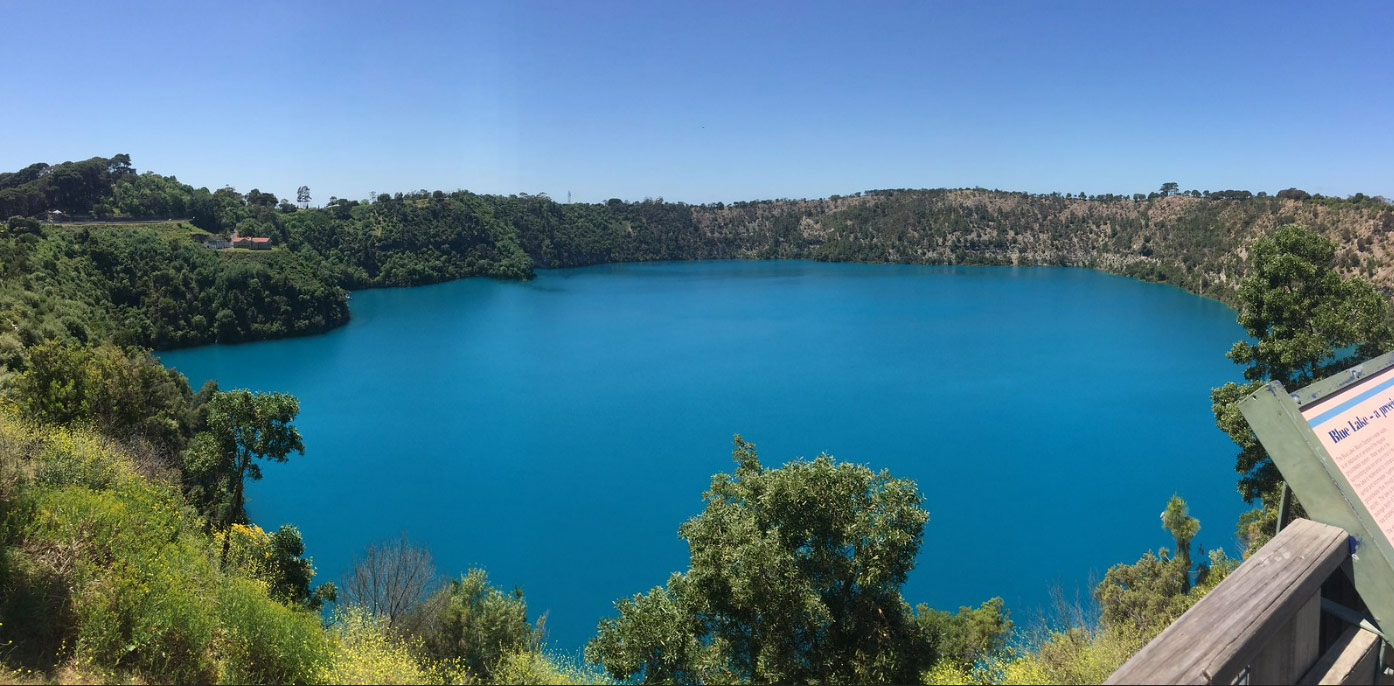 An image of a vibrant blue lake surrounded by trees and a viewing platform. The lake is inside of an extinct volcano crater