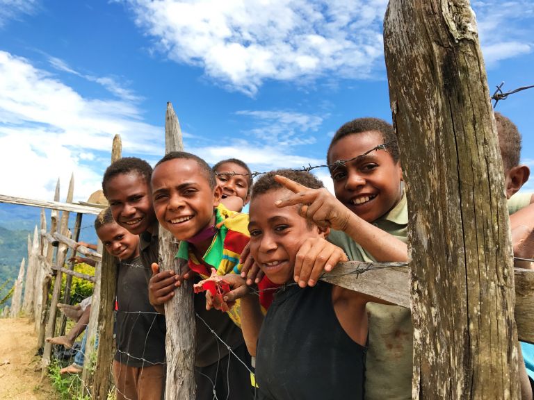 A group of smiling children standing along a barbwire fence in PNG