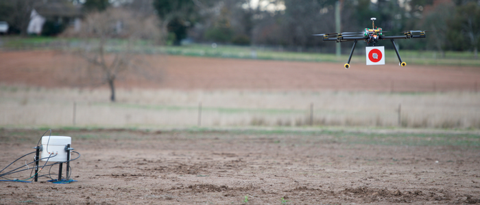 A drone being used as part of scientific experiment, with agricultural crop and trees in the background.
