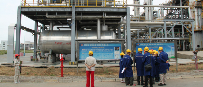 A group of people wearing safety equipment with industrial equipment in the background